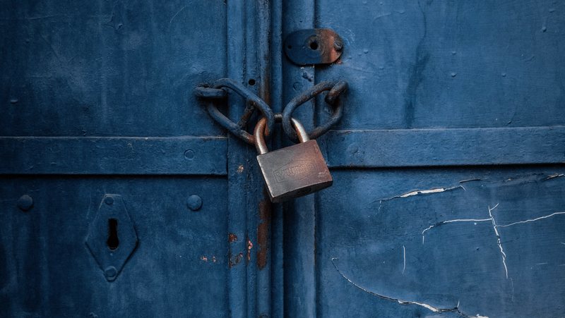 A rusted padlock and chain fastening a pair of weathered blue metal doors.