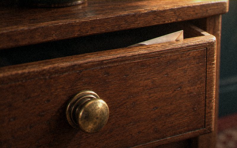 A folded paper note tucked into the gap of a half-open wooden drawer.